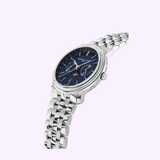 The Frederique Constant Index Business Timer FC-270N4P6B is a silver wristwatch with a metallic link band and deep blue multi-dial face, including a moon phase, shown at an angle on a light lavender background.