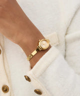 A person wears the Guess Watches GW0924L2 gold-tone bangle watch (UPC: 091661581229) with a round face and gold strap, styled in a textured white coat with gold buttons—a chic look for fans of Guess Watches.