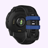 The Garmin Watches Instinct® 3 – 50 mm AMOLED 010-03020-03, shown from the back, features a green sensor light, “INSTINCT” branding on the backplate, and a black strap with two blue loops.