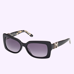 Showcasing Miami-inspired style, the Guess By Marciano Sunglasses GM00018 5601B feature a black rectangular frame with dark gradient lenses and gold accents, including a bold M on the temples. The inner arms are adorned with gold-detailed decorative patterns, reflecting the brand’s signature flair. These 100% authentic Guess By Marciano Sunglasses are set against a light purple background.
