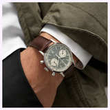 A person in a green jacket and white shirt wears the Hamilton Watches American Classic Intra-Matic Auto Chrono 40mm H38416560, featuring a panda dial, brown leather strap, and gray dial with two subdials.