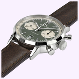 A close-up of the Hamilton Watches American Classic Intra-Matic Auto Chrono 40mm H38416560, featuring a green panda dial, two beige subdials, silver case, and brown leather strap, set against a light purple background.