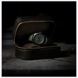 A Hamilton Watches Call of Duty: Modern Warfare 4 KHAKI FIELD H69469930 SPECIAL EDITION by Hamilton Watches, featuring a green fabric strap, is showcased in an open leather zippered case on a stone surface under dramatic lighting—an ideal piece for any Call of Duty: Modern Warfare 4 fan.