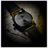 A close-up of the back of the Hamilton Watches Call of Duty: Modern Warfare 4 KHAKI FIELD H69469930 SPECIAL EDITION by Hamilton Watches reveals intricate engraved text and a wave pattern. The watch, shown with both leather and fabric straps, rests on a textured, cracked concrete surface marked with yellow lines—a style also showcased in Call of Duty: Modern Warfare 4.