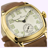 Hamilton Watches American Classic Cushion Mechanical gold cushion-shaped watch featuring a cream dial with luminescent Arabic numerals and a brown leather strap.