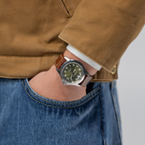Hamilton Watches H64475560 Khaki Field King Day-Date wristwatch with an olive green dial and a brown leather strap worn on a wrist.