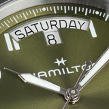 Close-up of a Hamilton Watches H64475560 Khaki Field King Day-Date green dial showing the day SATURDAY and the date 8 in a window at the top, with silver hands featuring white centers.
