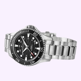 The Hamilton Watches H82415130 Khaki Navy Scuba Auto 40mm, a silver wristwatch with a black dial, white hour markers, and a metal bracelet, is shown at an angle on a light purple background.