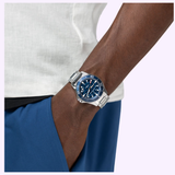 A person wearing blue pants and a white shirt has their hand in their pocket, showcasing a silver wristwatch with a blue face and white markings—the Hamilton Watches H82425140 Khaki Navy Scuba Auto 40 mm by Hamilton Watches.