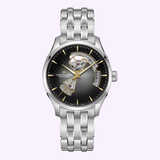 The Hamilton Watches Jazzmaster Open Heart Auto 40 mm H32675181 by Hamilton Watches is a striking silver wristwatch, showcased on a light background. It features a black and gold open-heart dial with visible gears, elegant silver hour markers, and a stainless steel link bracelet—an exquisite automatic dress watch designed to impress.