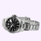 The Hamilton Watches Khaki Aviation Pilot Auto H76215130, featuring a 36mm stainless steel case, black dial with white numerals, and metal link band, is shown angled on a light purple background with its hands and minute markers clearly visible.