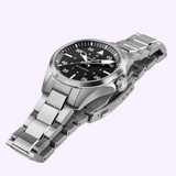 The Hamilton Watches Khaki Aviation Pilot Auto H76215130 features a stainless steel case, black dial with white numerals, metal link bracelet, and classic 36mm design, shown angled on a light purple background.