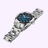 A Hamilton Watches Khaki Field Murph 38mm H70405140 wristwatch in stainless steel, featuring a blue-to-black 38mm dial with yellow hour markers and a silver metal link band, is showcased on a light purple background—an interstellar timepiece echoing the iconic design of the Hamilton Khaki Field Murph.