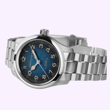 A Hamilton Watches Khaki Field Murph 38mm H70405140 wristwatch by Hamilton Watches, featuring a silver case, blue-to-black dial with Arabic numerals, and a metal link bracelet, is displayed against a light purple background, evoking the timeless appeal of the Interstellar watch.