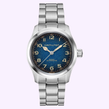 Showcasing the Hamilton Watches Khaki Field Murph 38mm H70405140, this stainless steel wristwatch features a distinctive blue-to-black 38mm dial with Arabic numerals, silver hands, and a sleek metal link bracelet. The Hamilton Watches brand name is prominently displayed on the face. Inspired by the iconic “interstellar” Khaki Field Murph, this timepiece is presented against a light purple background.