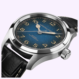 A Hamilton Watches Khaki Field Murph 38mm H70405740 with a silver case, textured blue dial, gold Arabic numerals, and black leather strap is angled to showcase the crown and case details.