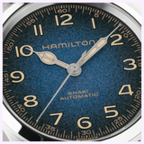 Close-up of the Hamilton Watches Khaki Field Murph 38mm H70405740 automatic watch face, set against a blue textured background. Gold numerals and gold hands point to 10:09, while the dial displays the Hamilton Watches brand name along with “Khaki,” “Automatic,” and “Swiss Made,” echoing the iconic Interstellar timepiece design.