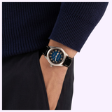 A person dressed in a navy sweater and dark pants has their hand in their pocket, displaying the Hamilton Watches Khaki Field Murph 38mm H70405740 automatic watch by Hamilton Watches, featuring a blue dial and black leather strap.