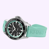 The Hamilton Watches Khaki Navy Scuba 40mm H82415331 features a silver and black case, black dial, mint green "KHAKI" rubber strap, white hour markers, and rotating bezel. Brand: Hamilton Watches. Background is light purple.