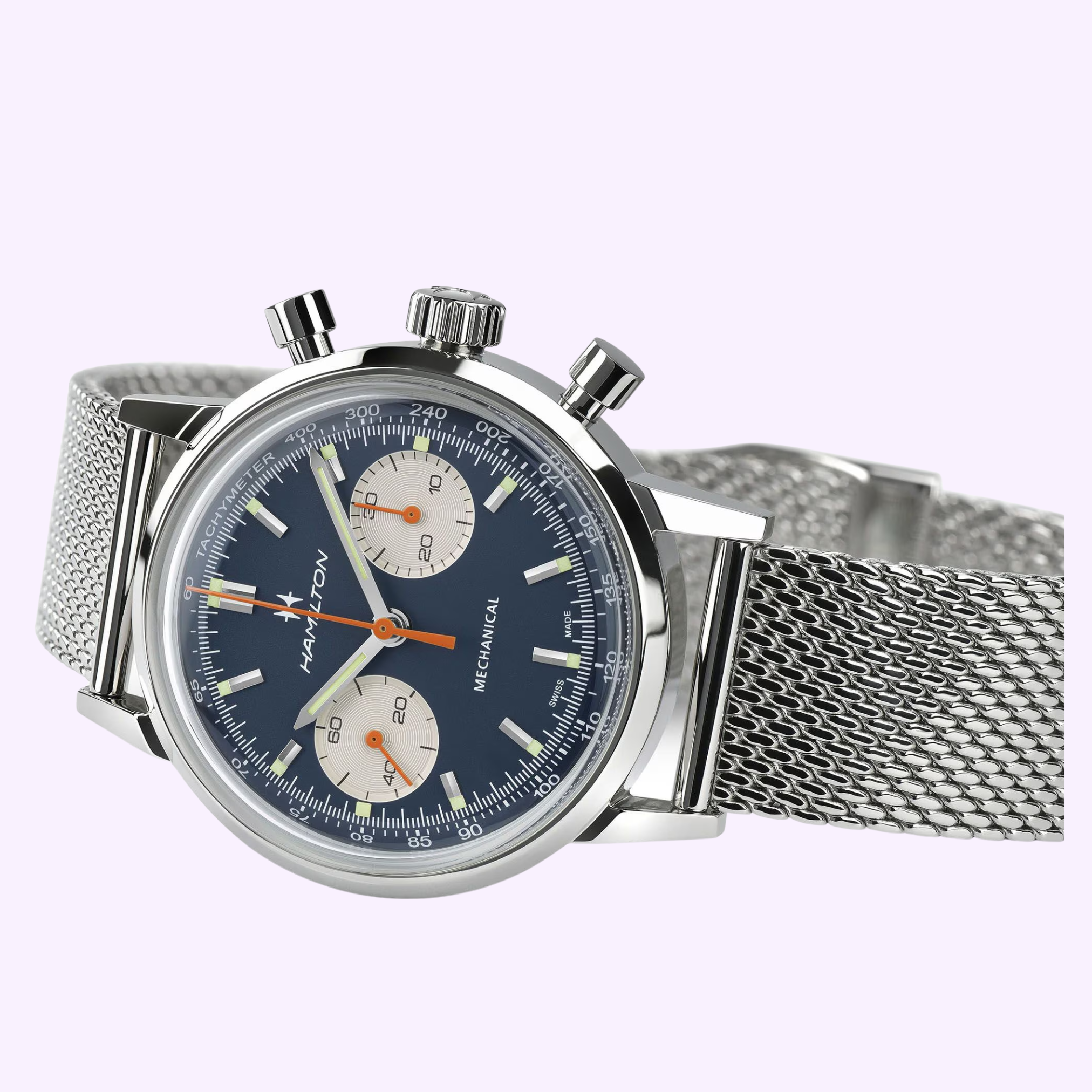 The Hamilton Watches American Classic Intra-matic Chronograph H38429541 features a 40mm case, blue dial with two white subdials, silver hour markers, and a stainless steel mesh strap, displayed on a light purple background.
