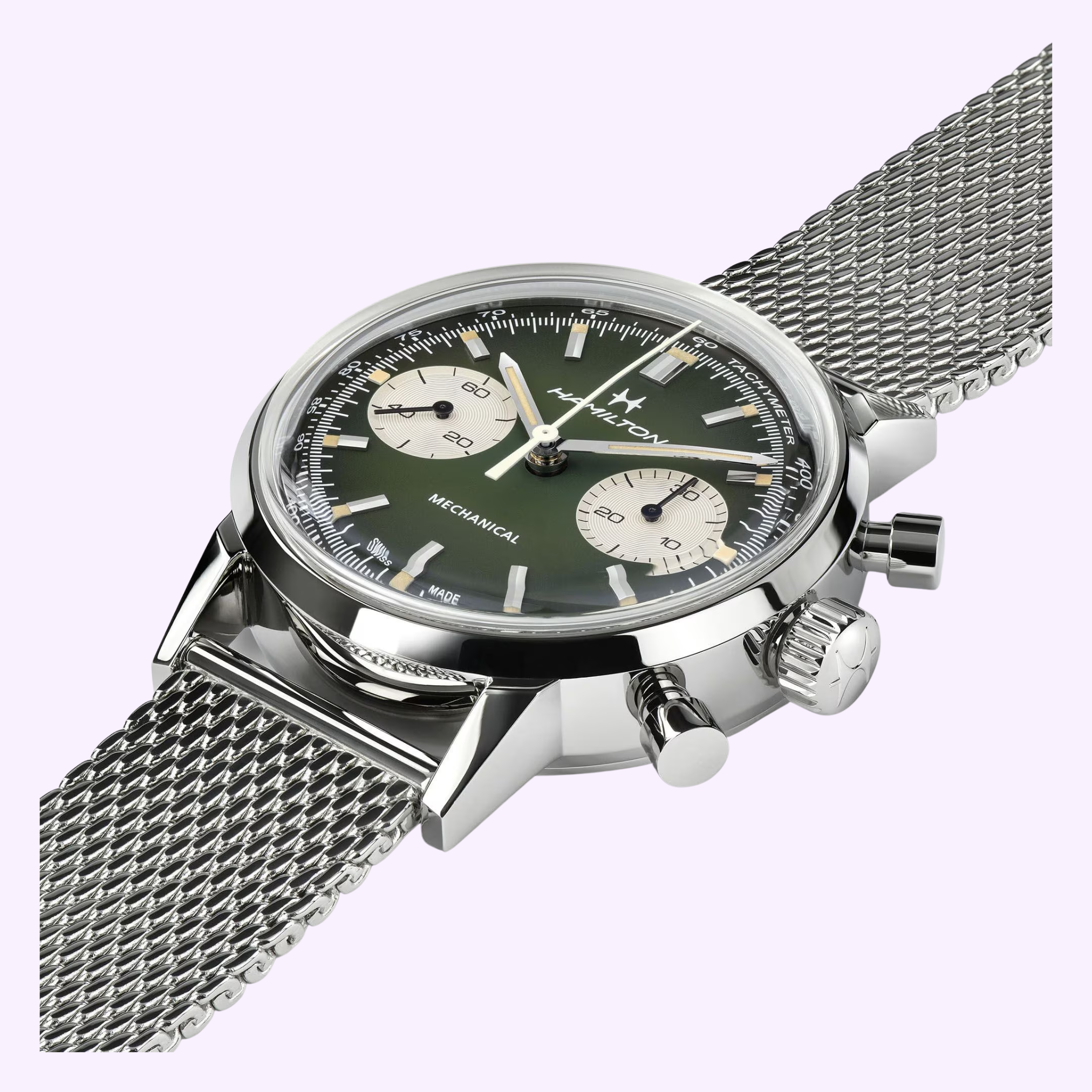 A close-up of the Hamilton Watches American Classic Intra-matic Chronograph H38429861 with a green dial, white subdials, silver mesh band, and two side buttons, set against a pale purple background—a true American Classic.
