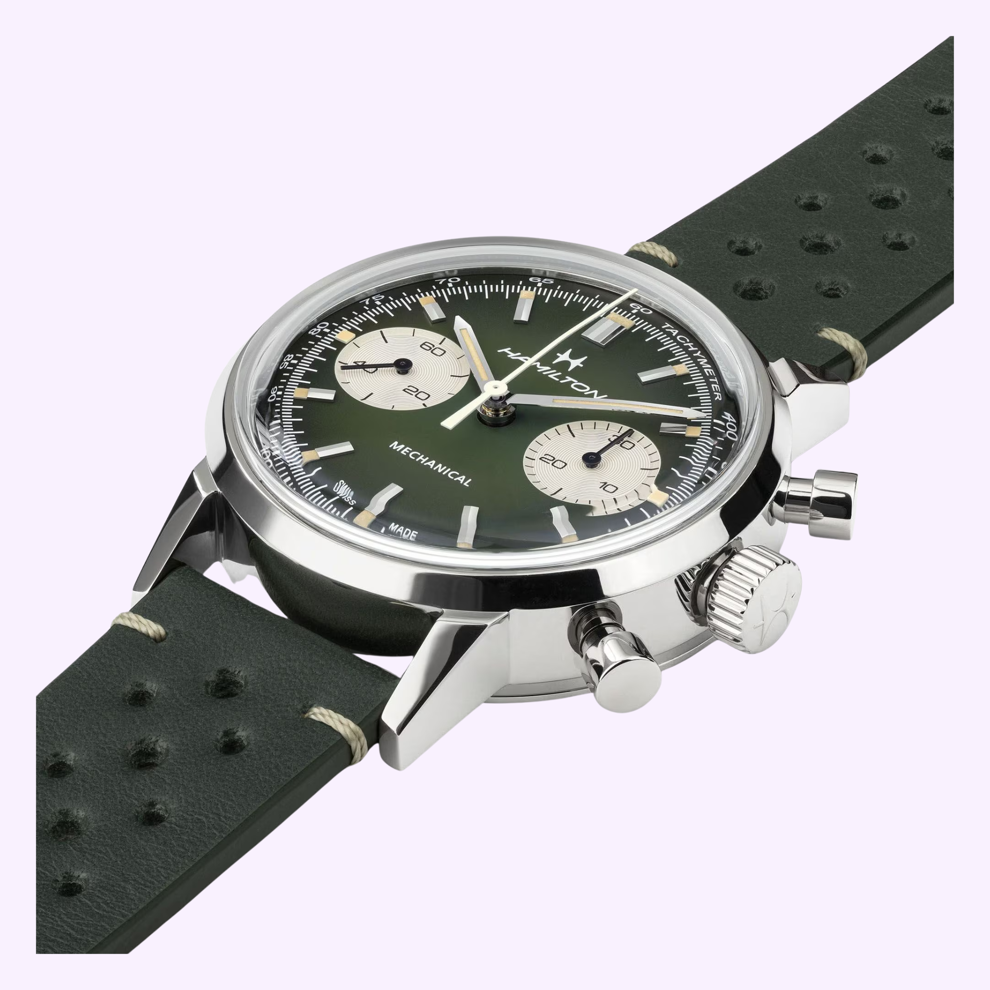 A close-up of the Hamilton Watches American Classic Intra-matic Chronograph H38429861, featuring a green dial, two subdials, stainless steel case, and perforated dark green leather strap against a light purple background.