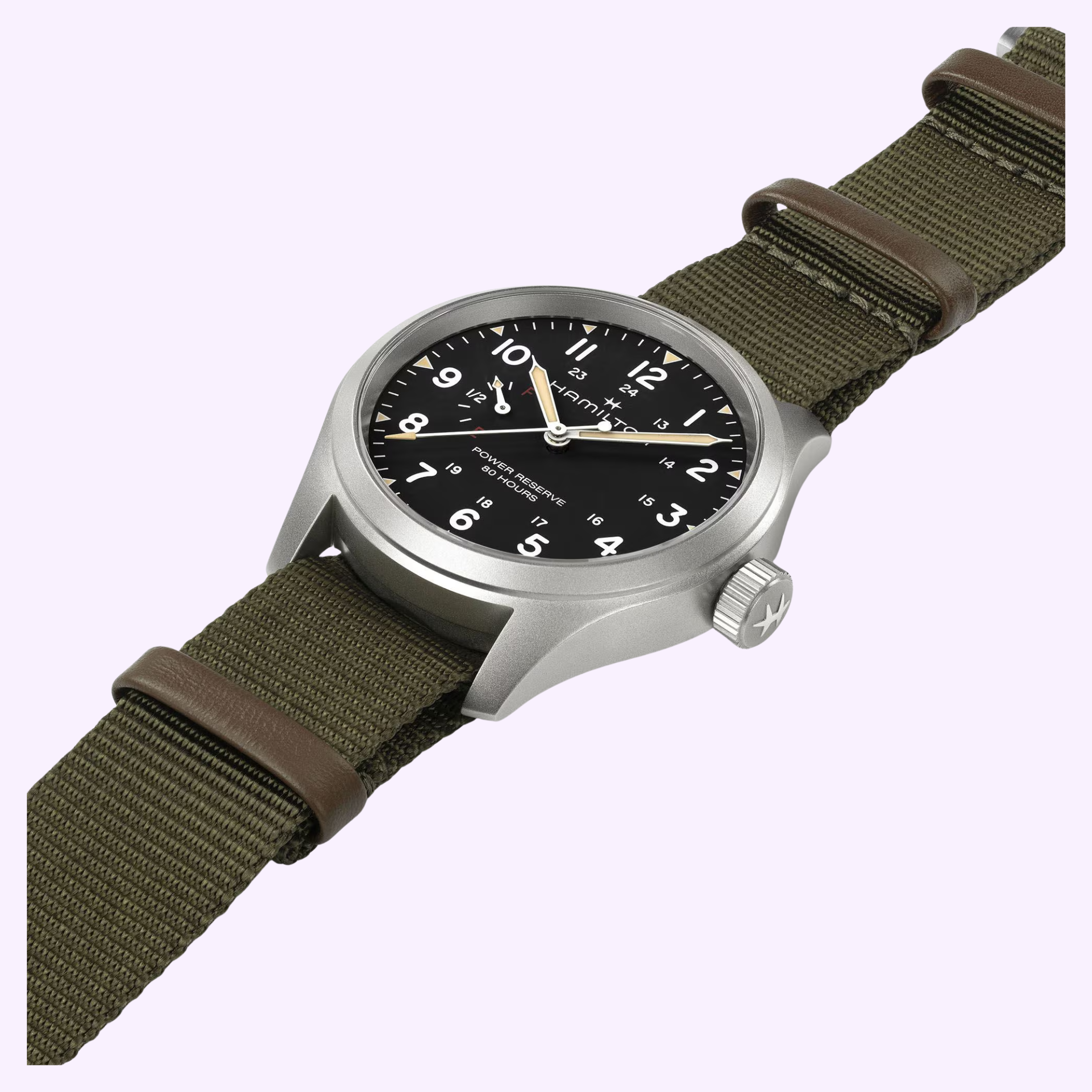 The Hamilton Watches Khaki Field Mechanical Power Reserve 40 mm H69509930 features a stainless steel case, black dial with white numerals, green fabric strap with brown leather accents, and boasts an 80-hour power reserve. Displayed on light purple.