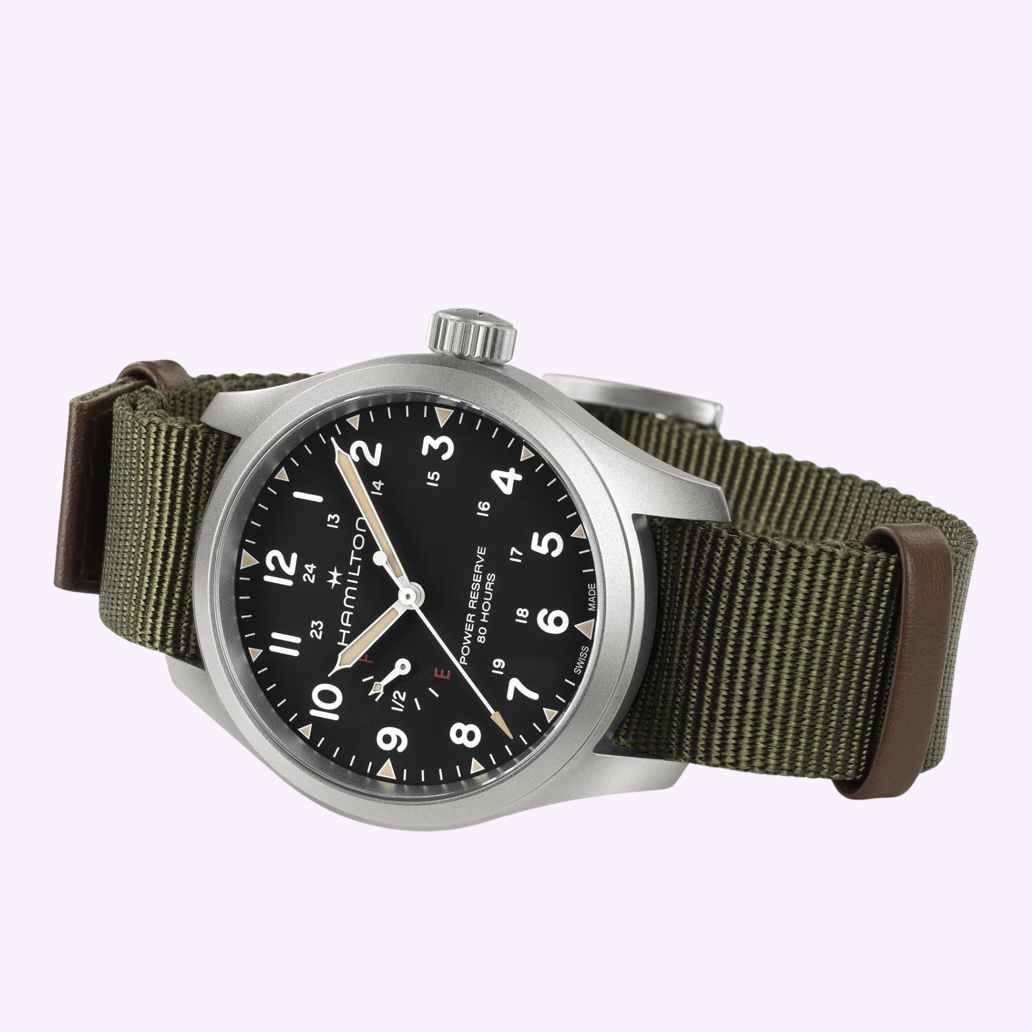 The Hamilton Watches Khaki Field Mechanical Power Reserve 40 mm H69509930 features a black dial with white numerals, a silver case, and an olive green fabric strap with brown leather accents, shown on a light purple background.