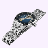 The Hamilton Watches Jazzmaster Open Heart Auto H32675140 is a luxury stainless steel automatic watch with a blue gradient dial, open-heart movement, and polished bracelet, showcased at an angle on a light background.