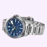 The Hamilton Watches Khaki Aviation Pilot Auto 39mm H76305140 features a stainless steel case, blue dial with white hour and minute markings, and a metal link bracelet, shown against a light purple background.