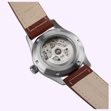A close-up of the back of a Hamilton Watches Khaki Field Auto 38 mm H70455540 highlights its intricate automatic movement through a transparent caseback, while the brown leather strap features detailed stitching and signature branding.