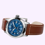 The Hamilton Watches Khaki Field Auto 38 mm H70455540 features a 38mm stainless steel case with a blue dial, white numerals, a date window, and a brown leather strap with white stitching, showcased against a light background.