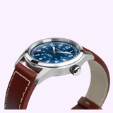 The Hamilton Watches Khaki Field Auto 38mm (H70455540) features a silver-tone case, striking blue dial with white numerals, date window, and a brown leather strap, displayed on a light background.