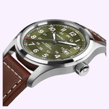 A close-up of the Hamilton Watches Khaki Field Auto 42mm H70605560, featuring a green dial, white numerals, date display, stainless steel case, and brown leather strap with white stitching. The crown bears the Hamilton logo.