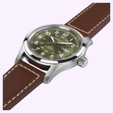 The Hamilton Watches Khaki Field Auto 42mm H70605560 features a brown leather strap, stainless steel case, olive green dial with white Arabic numerals and hands, plus a date window at 3 o’clock.