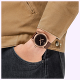Wearing a Hamilton Watches Khaki Field Auto The Odyssey Limited Edition H70675530, featuring a bronze case, dark dial, and brown leather strap, paired with a tan jacket and dark jeans, one hand casually in their pocket.