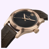 The Hamilton Watches Khaki Field Auto The Odyssey Limited Edition H70675530 features a gold-tone case, black dial with gold markers, and brown leather strap. Inspired by the Christopher Nolan watch, the Hamilton brand is visible on the face.