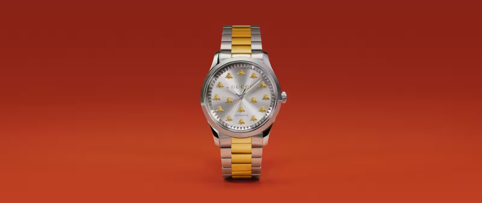 A silver and gold Gucci wristwatch with a metallic band, displayed upright against a solid orange background. The watch face features gold bee motifs in place of traditional numerals.