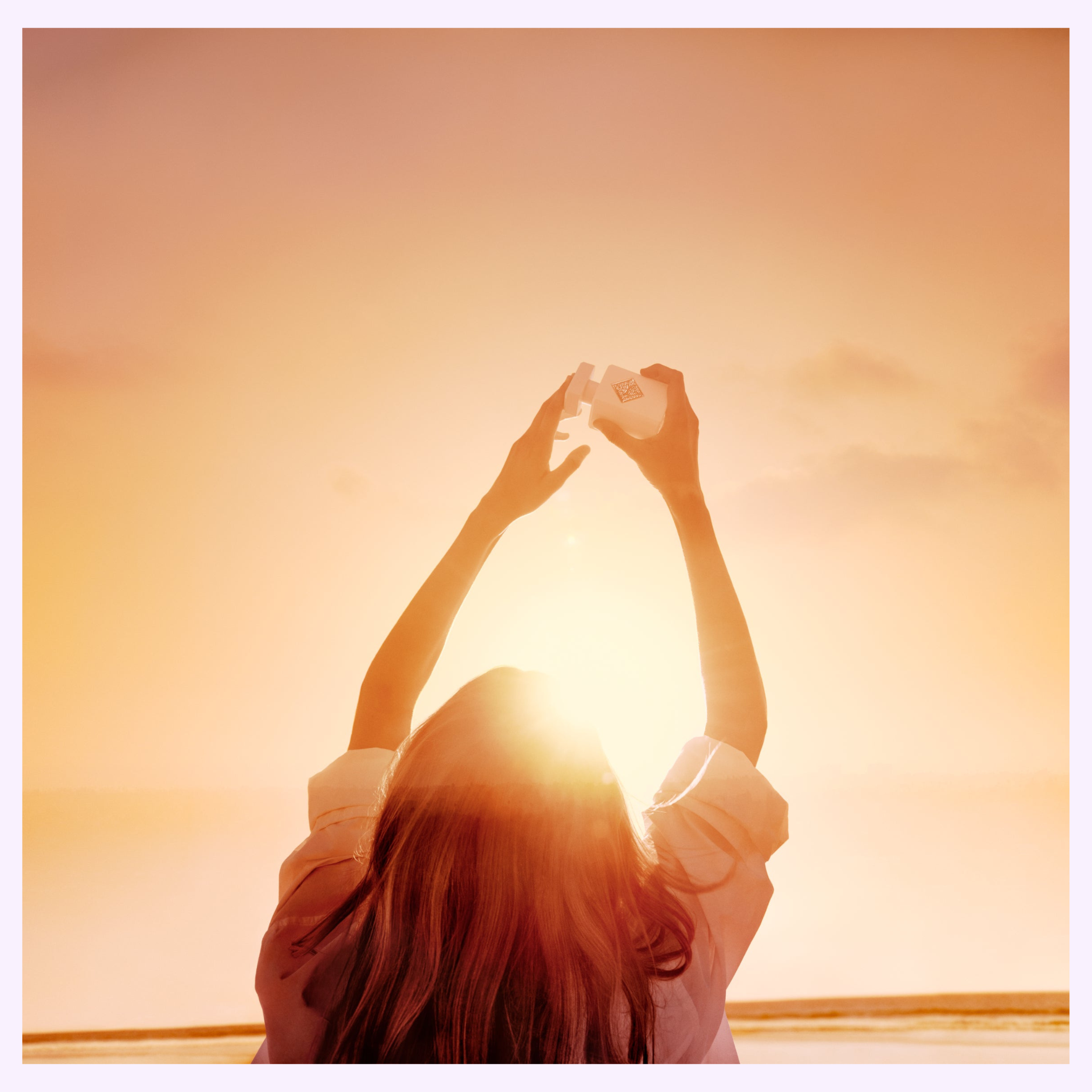 A woman with long hair faces a bright sunrise, holding a house-shaped object before the sun. Warm orange and yellow hues echo the vibrant spirit of Initio Perfumes LIFT ME UP Extrait de Parfum 3.0 Oz for women.