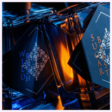 Close-up of two glass Initio Perfumes bottles, including the INITIO Parfums Prives WILD RUSH EDP 3.0 Oz Unisex Perfume, with dark ornate labels and dramatic elegance in warm orange and blue light.