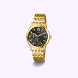 The Guess Watches GW0976G2 features a gold tone, black dial with gold hour markers, multiple subdials, and a polished recycled steel bracelet that stands out against a pale background.