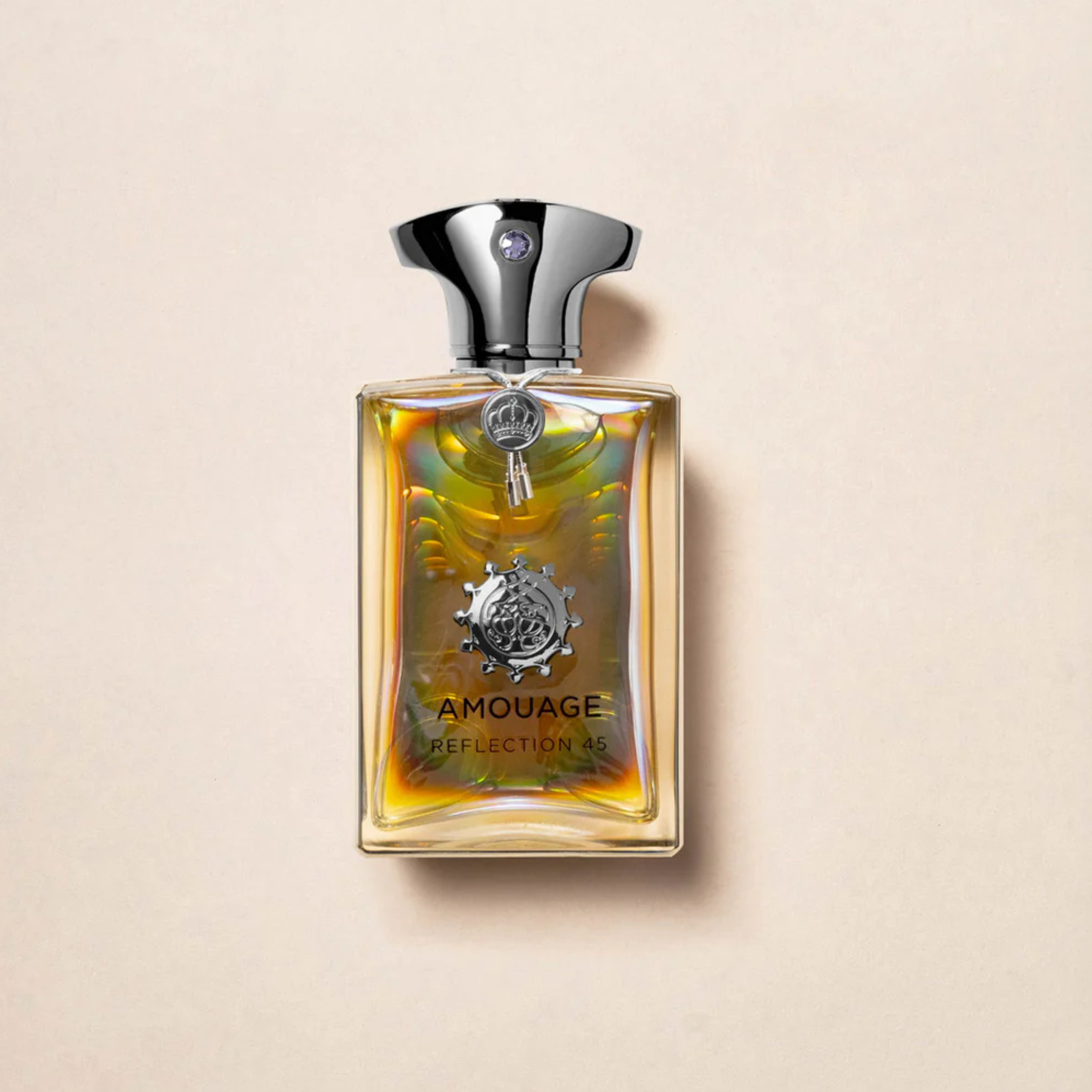 A rectangular glass bottle with a silver cap holds AMOUAGE Reflection 45 3.4 Oz Men Perfume, featuring a golden liquid and label with a silver emblem, evoking luxurious woody-musky-floral notes on a beige background.