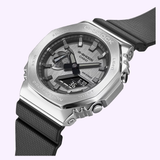 The G-Shock Watches CASIO G-STEEL GM-2100-1ASW features a silver bezel, black strap, analog-digital display, and side buttons, showcased at an angle on a pale purple background.