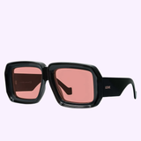 Loewe LW40064U 01Y Unisex Sunglasses by Loewe Sunglasses, featuring chunky black square frames and rose-tinted lenses with the LOEWE brand name in white on the left arm, are displayed against a light purple background. These stylish sunglasses are available from an authorized Miami dealer.