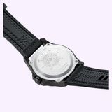 A close-up of the back of the Luminox Watches Atacama Field XL.1971.SET, featuring a metal case back engraved with a compass design, black textured strap, and various numbers and text. The background is light purple.