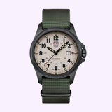 The Luminox Watches Atacama Field XL.1971.SET is a rugged 43mm field watch with a beige dial, black numerals, green fabric strap, date window at 3 o’clock, and the Luminox logo below 12, set against a light purple background.