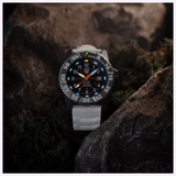 The Luminox Watches MIL-SPEC XL.3359.SET, a rugged black wristwatch with a grey strap, rests on rocks among moss. Its glowing white, blue, and orange dial details highlight the 300-meter water resistance by Luminox Watches.