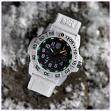 The Luminox Watches Navy SEAL 3500 XS.3507.WB, a rugged white military dive watch with a black dial and glowing green-orange markers, sits wet on a snow-dusted rock. Water droplets highlight its endurance.