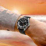 By the Miami ocean at sunset, a person stands wearing the Mido Watches Ocean Star GMT M0266291705101, featuring a black dial and strap.