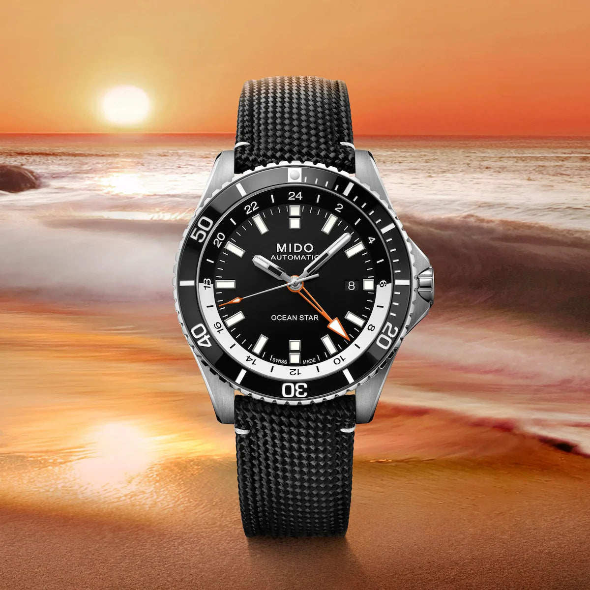 The Mido Watches Ocean Star GMT M0266291705101, featuring a black strap and dial, is showcased against a vivid Miami sunset by the ocean, with gentle waves meeting the shore.